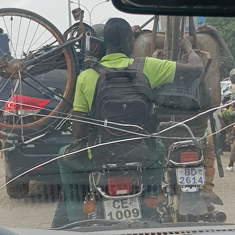 Moto-taxis on every corner carry all sorts of things: one holds a bicycle, the other a wheelbarrow on his head
